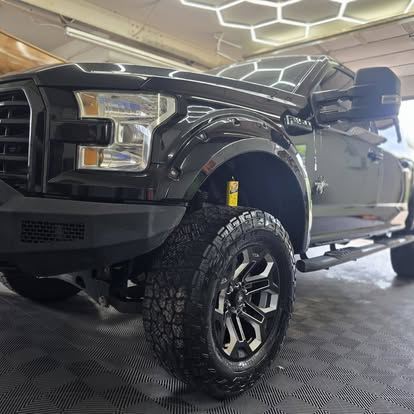 Lifted black Ford F-150 under hex shop lighting after tint work