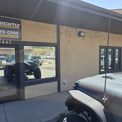 Tinted storefront glass reflecting a lifted Jeep outside a Cañon City shop