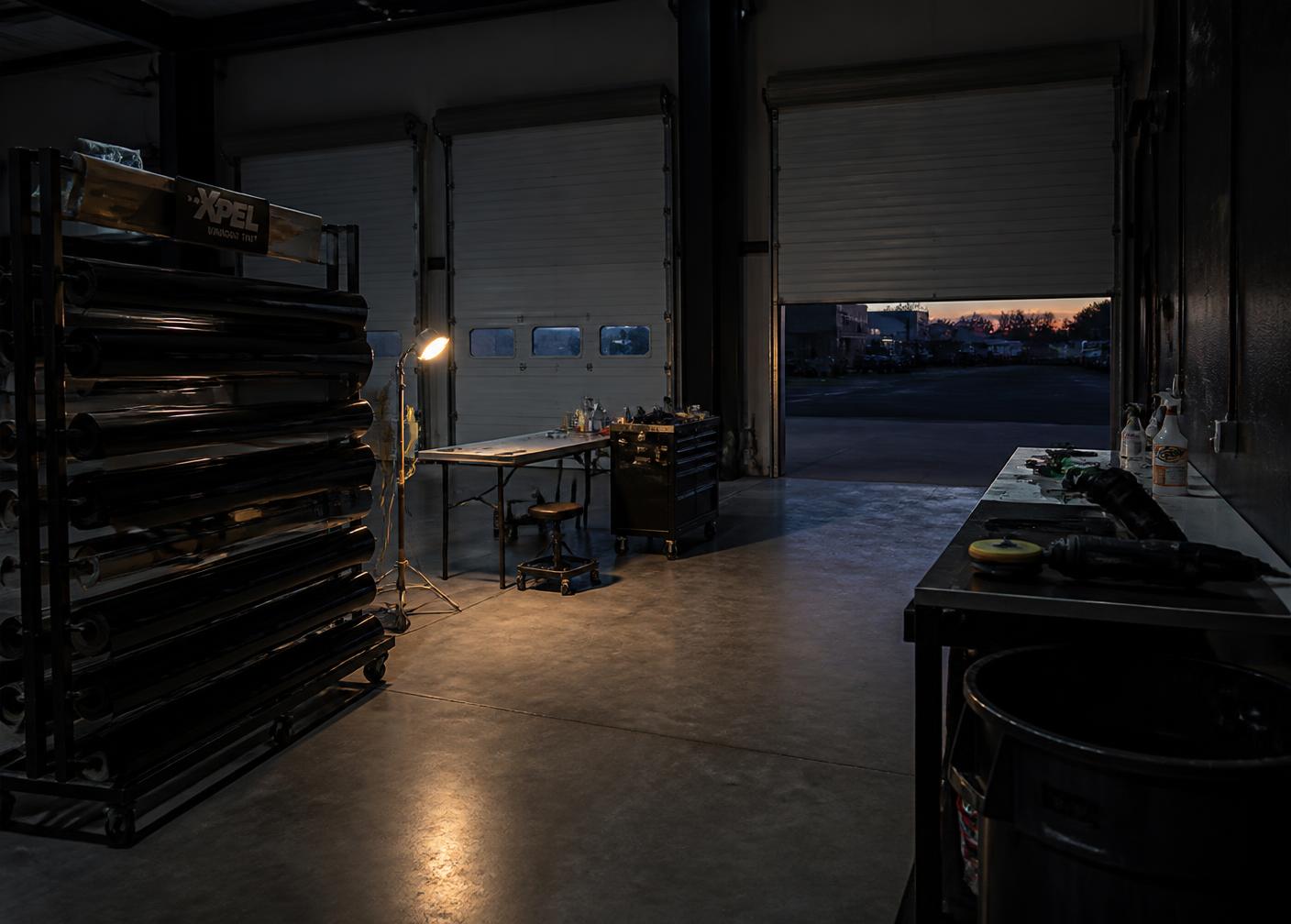 Rolls of window tint film on a rack inside a three-bay garage at dusk